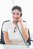 Businesswoman sitting at her desk on the phone smiling at camera
