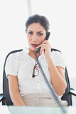 Serious businesswoman sitting at her desk on the phone