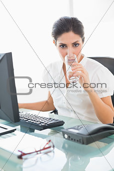 Stern businesswoman drinking a glass of water at her desk