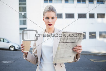 Serious stylish businesswoman holding newspaper and coffee
