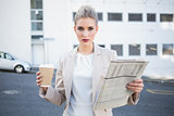 Stern stylish businesswoman holding newspaper and coffee