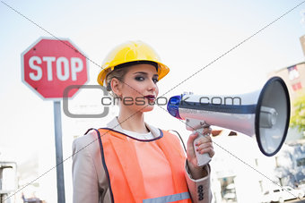 Serious businesswoman wearing builders clothes holding megaphone