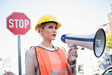 Frowning businesswoman wearing builders clothes holding megaphone