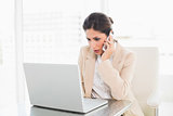 Frowning businesswoman working with a laptop on the phone