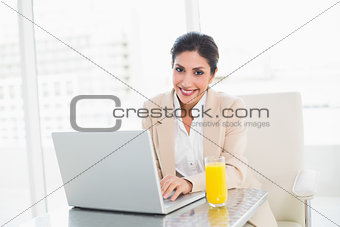 Happy businesswoman with laptop and glass of orange juice at desk