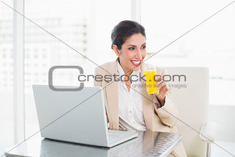 Smiling businesswoman with laptop and glass of orange juice at desk