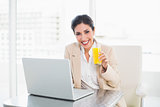 Cheerful businesswoman with laptop and glass of orange juice at desk