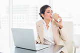 Stylish businesswoman drinking coffee while working on laptop