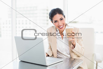 Happy businesswoman drinking coffee while working on laptop