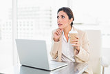 Thoughtful businesswoman drinking coffee while working on laptop