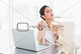 Thinking businesswoman drinking coffee while working on laptop