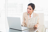 Happy businesswoman reading newspaper while working on laptop