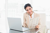 Smiling businesswoman holding newspaper while working on laptop
