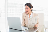 Cheerful businesswoman holding newspaper while working on laptop