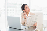 Stern businesswoman holding newspaper while working on laptop looking away