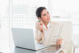 Smiling businesswoman holding newspaper while working on laptop looking away