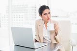 Smiling businesswoman holding mug while working on laptop