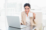 Happy businesswoman holding mug while working on laptop