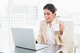 Cheerful businesswoman holding mug while working on laptop