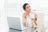 Thoughtful businesswoman holding mug while working on laptop