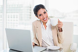 Happy businesswoman holding cup while working on laptop