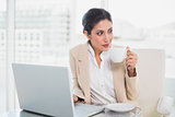 Thinking businesswoman holding cup while working on laptop