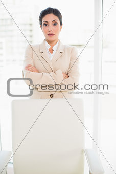Serious businesswoman standing behind her chair