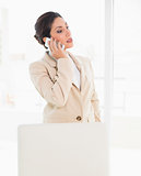 Frowning businesswoman standing behind her chair on the phone