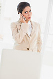Frowning businesswoman standing behind her chair on the phone looking at camera