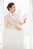 Businesswoman standing behind her chair holding tablet pc