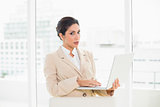 Frowning businesswoman standing behind her chair holding laptop