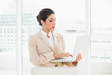 Serious businesswoman standing behind her chair holding laptop
