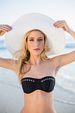 Serious sensual blonde in elegant black bikini wearing straw hat