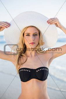 Serious sensual blonde in elegant black bikini wearing straw hat