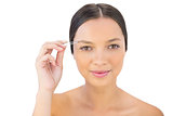 Cheerful natural woman using tweezers for her eyebrow