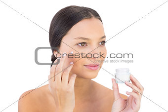 Brunette woman spreading beauty cream on her cheek