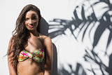 Smiling woman in bikini leaning against a wall