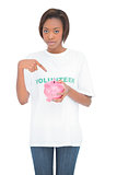 Serious volunteer woman pointing at her piggy bank