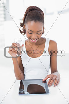Happy sporty model holding glass of water using tablet pc