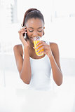Happy athletic woman phoning while drinking orange juice