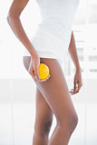 Mid section of sporty woman holding orange by her legs