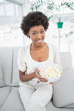 Attractive brunette holding popcorn sitting on cosy sofa