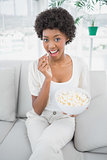 Attractive brunette eating popcorn sitting on cosy sofa