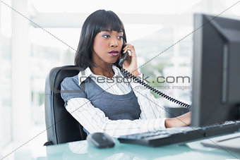 Serious businesswoman on the phone while working on computer