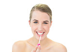 Cheerful attractive blonde applying pink lip gloss