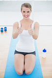 Smiling sporty woman on her knees giving thumbs up to camera