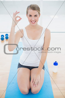 Smiling sporty woman on her knees giving okay gesture