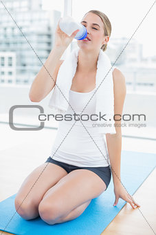 Fit woman on her knees on sport mat drinking water