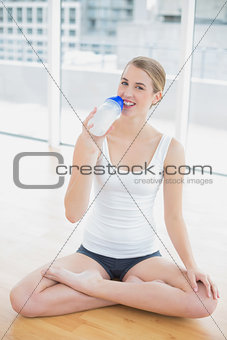 Smiling fit woman in lotus position holding flask