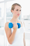 Pensive fit woman exercising with dumbbells